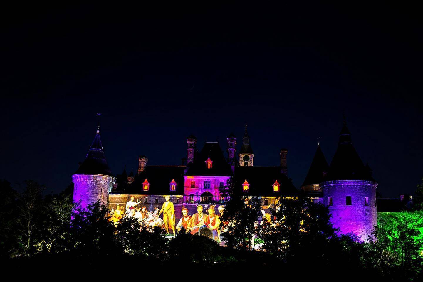 Château médiéval avec projecteurs colorés et silhouettes lumineuses